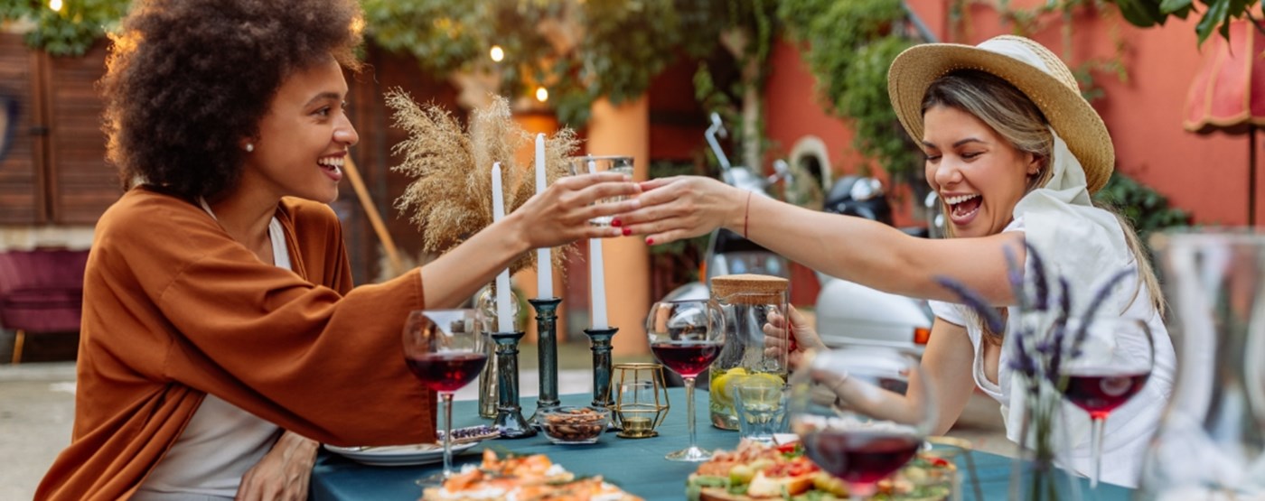 Two women exchanging a glass while seated at a picnic table 